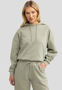 Hellgrüner Kapuzenpullover mit Kordelzug, lässigem Schnitt und gesticktem Logo; kombiniert mit passenden Jogginghosen mit elastischem Bund.