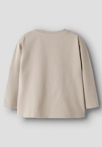 Vaalea beige pitkähihaisesta puuvillapaidasta, jossa on pyöreä kaula-aukko, näkyy selkäpuolelta vaalean harmaan taustan kanssa.