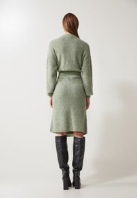 Robe tricotée verte au design ajusté, longueur mi-mollet et manches longues. Associée à des bottes noires en cuir montantes.