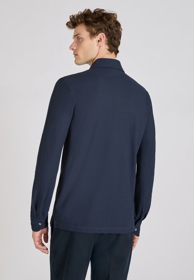 Marineblauwe longsleeve shirt met een rechte kraag, gladde stof, zijsplitten aan de onderkant en knoopdetails bij de mouwen.