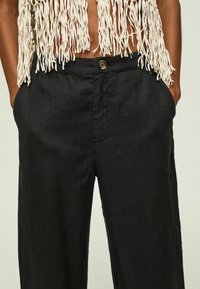 Czarne lniane spodnie o szerokich nogawkach z zapięciem na guzik z przodu i bocznymi kieszeniami, o gładkiej strukturze i luźnym kroju.