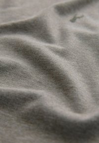 Gray cotton fabric with visible texture and gentle folds; features a small green embroidered accent.