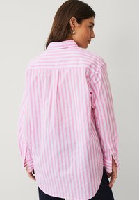Chemise à manches longues rayée rose et blanche avec un pli au dos, un poignet ouvert et un col boutonné ; fabriquée en tissu léger.
