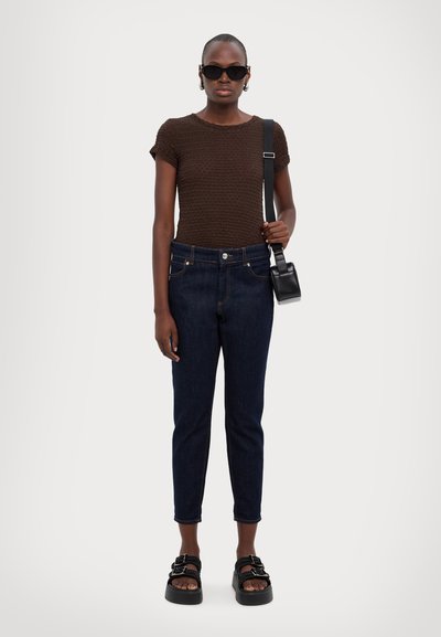 Καφέ πλεκτό τοπ με υφή, σκούρα μπλε τζιν σε στενή γραμμή, μαύρες πλατφόρμες σανδάλια με πόρπες και μια μικρή μαύρη τσάντα χιαστί.