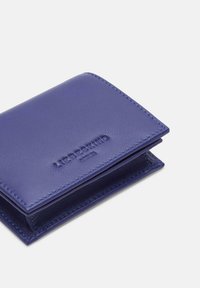 Portefeuille en cuir violet avec une texture lisse, présentant un logo en relief à l'avant, des bords cousus et un design compact et rectangulaire.