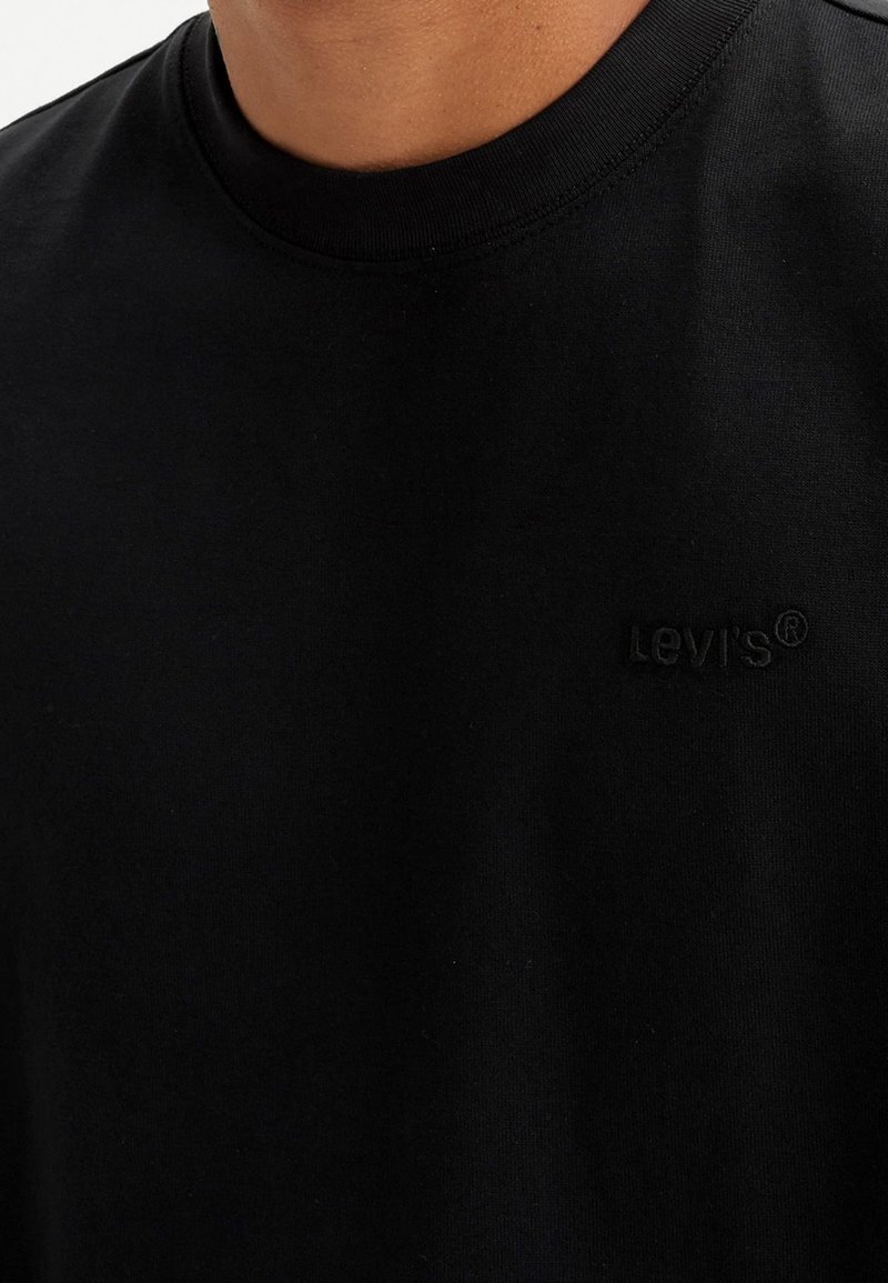 T-shirt en coton noir avec un col rond et des manches courtes. Présente un logo Levi's en relief discret sur la poitrine. Texture lisse.