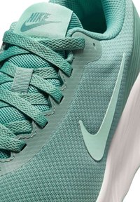 Nike-skor med en texturerad, mintgrön meshtopp, platta snören och en framträdande vit swoosh-logotyp på sidan. Gummisulan är synlig.