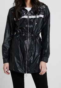 Černá, lehká bunda s krajkovým detailem na ramenním výstřihu, stříbrným zipem, stahovacími šňůrkami v pase a elastickými manžetami; lesklá textura.