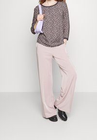 Top trasparente nero a fantasia floreale con maniche a 3/4, abbinato a pantaloni a gamba larga rosa chiaro e scarpe chunky nere. Borsa viola chiaro.