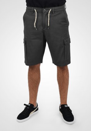 Shorts cargo en coton gris foncé avec une taille à cordon, deux poches latérales et une texture lisse. Associés à des baskets noires.