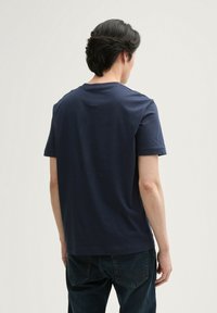 Tricou din bumbac de culoare bleumarin, cu mâneci scurte, guler clasic și un design minimalist. Textură moale cu o croială lejeră.