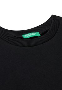 Detailní záběr černého svetr s kulatým výstřihem, ve kterém je uvnitř límce přišitá zelená etiketa "United Colors of Benetton".