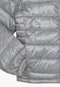 Giacca a vento grigia con dettagli multicolore, sezioni trapuntate e polsini elasticizzati. Texture liscia con una finitura lucida.