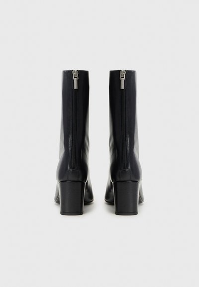 Svarta läderankelboots med rak design, blockklack och dragkedja bak. Slät textur med minimal detaljering.