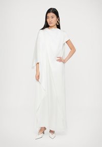 Bijela, lepršava maxi haljina s naboranim dizajnom i kratkim rukavima. Glatki materijal s asimetričnim rubom. Dopunjena šiljastim bijelim cipelama.