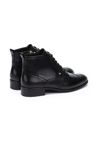 Botas de tobillo de cuero negro con diseño de cordones, detalles de brogue y un tacón bajo tipo bloque. Textura suave y herrajes en dorado.