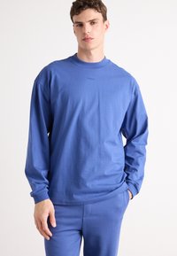 Blue long-sleeve shirt made of cotton, featuring a round neckline and relaxed fit. The brand logo is subtly displayed on the chest.