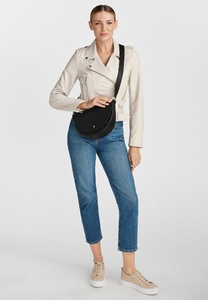 Czarna torba na ramię o zaokrąglonym kształcie i gładkiej fakturze, w połączeniu z beżową skórzaną kurtką i jasnoniebieskimi dżinsami.