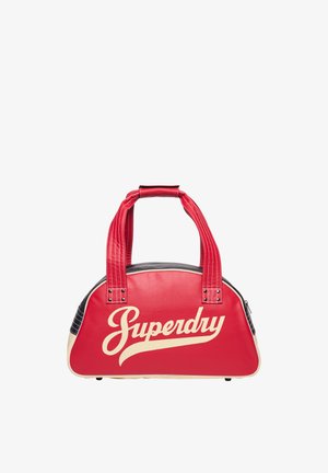 Bolso Superdry rojo y crema con dos asas rojas y un ribete negro y crema sobre un fondo blanco.