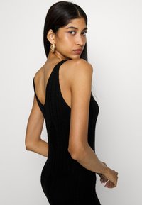 Black knitted dress with a ribbed texture, featuring thick shoulder straps and a deep V-back design, highlighting a form-fitting silhouette.