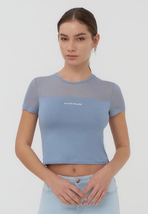 T-shirt cropped azzurro chiaro con parte superiore in rete, maniche corte e testo "falo per la trama" al centro. Texture liscia.