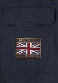 Námorná látka so znakem britské vlajky a nápisem "HACKETT LONDON" vyšitým zlatou nití. Obsahuje design kapsy.