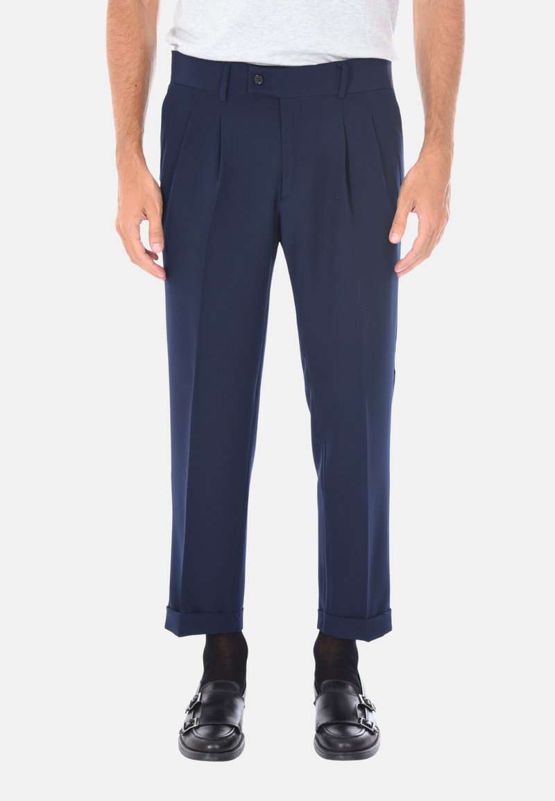 Pantaloni a pieghe blu navy realizzati in un tessuto liscio, dotati di chiusura con bottone e di risvolti alla caviglia, abbinati a scarpe nere.