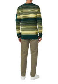 Gebreide trui met groene en gele horizontale strepen, ronde halslijn en lange mouwen; gecombineerd met lichtbeige broek en witte sneakers.
