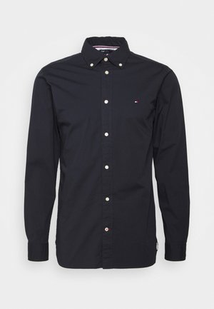 Dunkelblaue Hemdbluse mit Kragen, weißer Knöpfe und einem kleinen Logo auf der Brust. Hergestellt aus glattem Stoff mit langen Ärmeln.