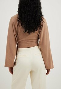 Brun ribbet crop top med lange ærmer parret med cremede skræddersyede bukser med sidelommer og en glat overflade.