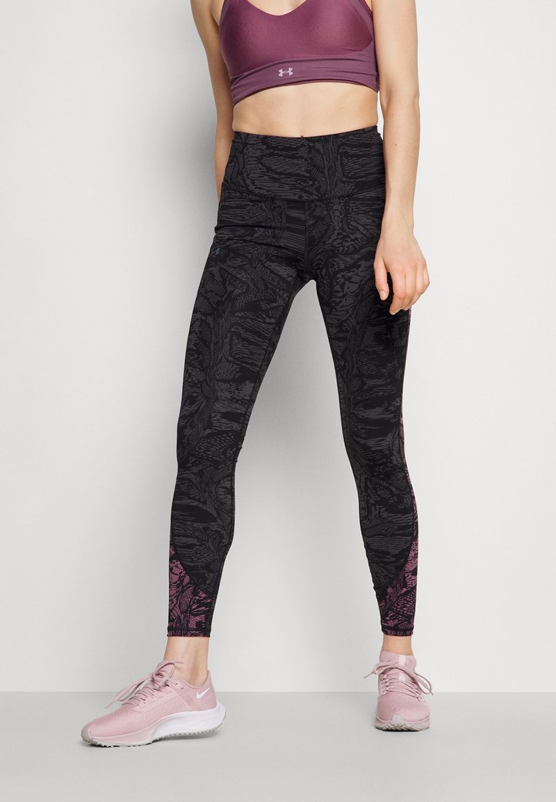 Schwarze, hochtaillierte Leggings mit strukturiertem Muster, die rosa Akzente an den Knöcheln aufweisen und mit einem lila Sport-BH sowie hellrosa Sneakers kombiniert sind.