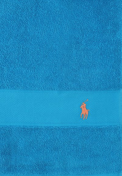 Φωτεινή μπλε πετσέτα με υφή και οριζόντια ταινία που φέρει πορτοκαλί κέντημα ενός παίκτη πόλο πάνω σε άλογο.