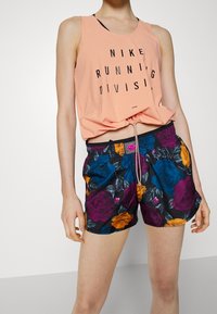 Canotta rosa Nike con testo nero e pantaloni corti floreali neri con motivi di rose vibranti in viola, blu e arancione. Vita elastica con cordoncino.