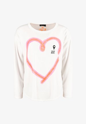 White long-sleeve shirt featuring a pink sequined heart design and the text "YOU ARE HERE". Rounded neckline with a relaxed fit.