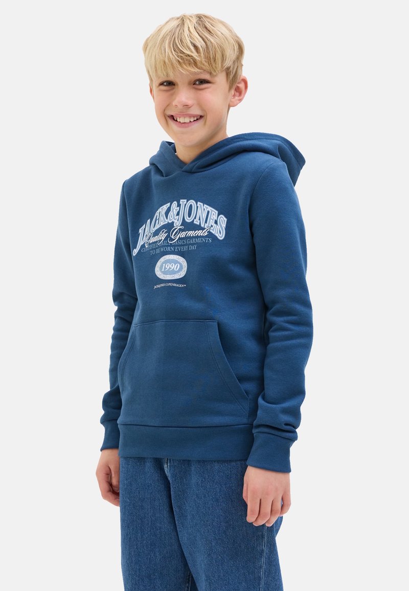 Hoodie en coton bleu avec une poche kangourou, des poignets côtelés et une capuche à cordon. Présente une impression graphique blanche sur le devant. Porté avec un jean bleu.