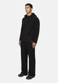 Hoodie in fleece nero e pantaloni coordinati, caratterizzati da una superficie testurizzata, vestibilità ampia, tasca frontale e dettagli del logo discreti.