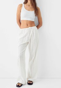 Vita, lätta byxor med spetsdesign och dragsko i midjan. Kombineras med en åtsittande vit linne och svarta slip-in sandaler.