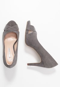 Šedé semišové lodičky na vysokém podpatku s otevřenou špičkou a detaily křížových popruhů. Úzký podpatek a hladká vnitřní podšívka.