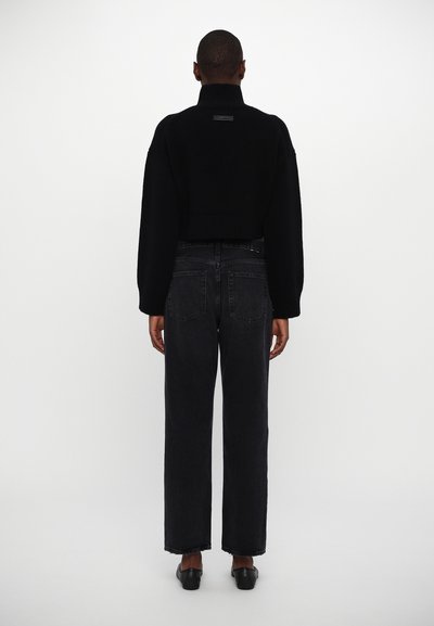 Black cropped sweater with a high collar and ribbed hem, paired with high-waisted dark denim jeans and black slip-on shoes.