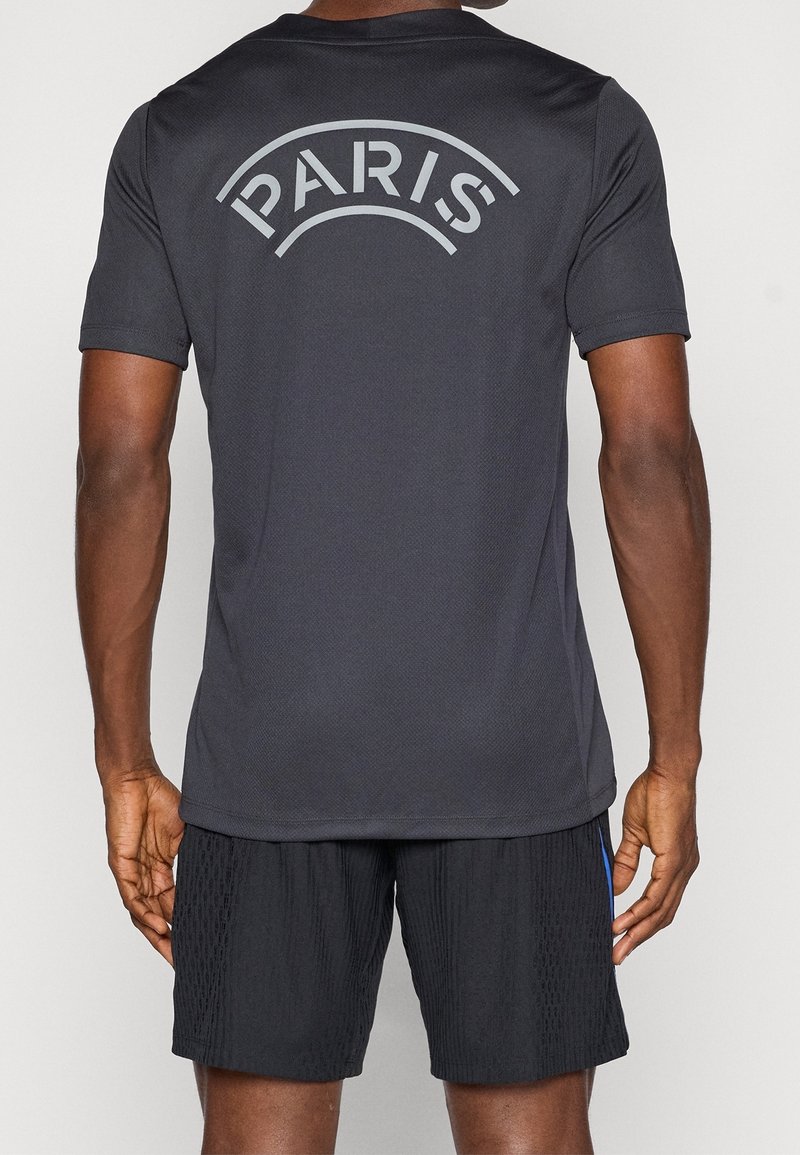 Personne portant un t-shirt noir à manches courtes avec "PARIS" imprimé en grosses lettres dans le haut du dos et un short noir.