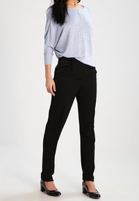 Maglione azzurro chiaro, morbido e ampio, con colletto rotondo e maniche lunghe, abbinato a pantaloni neri e tacchi neri. Tessuto liscio, design lineare.
