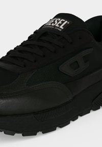 Μαύρο sneaker Diesel με υφασμάτινο και δερμάτινο ανιμαρισμένο επάνω μέρος, μαύρα κορδόνια, χοντρή σόλα και το λογότυπο Diesel στη γλώσσα και στην πλαϊνή πλευρά.