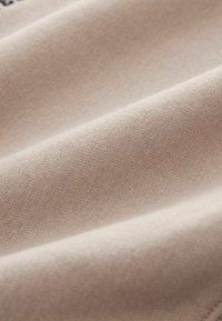 Helles beige Gewebe mit glatter Textur, das leicht dehnbar ist und eine feine Webart aufweist, mit sanften, subtilen Farbvariationen.