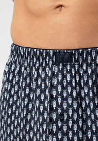 Boxer bleu marine avec un motif bleu clair de petites figures, doté d'une taille élastique et d'un détail avec un seul bouton à l'avant.