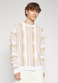 Ljusbeige och krämrandig tröja med strukturerade mönster, rund halsringning och ribbade muddarna, tillverkad av ett stickat tyg.