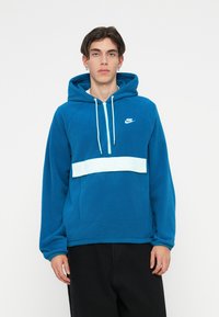 Zila flīsa kapuce ar priekšējo kabatu, baltu horizontālu svītru un regulējamu kapuci ar montāžu. Nike logo uz krūtīm.