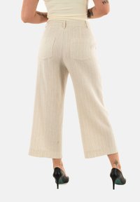 Pantaloni ampi beige a righe con vita alta, due tasche posteriori e un tessuto testurizzato, abbinati a scarpe con tacco nere.