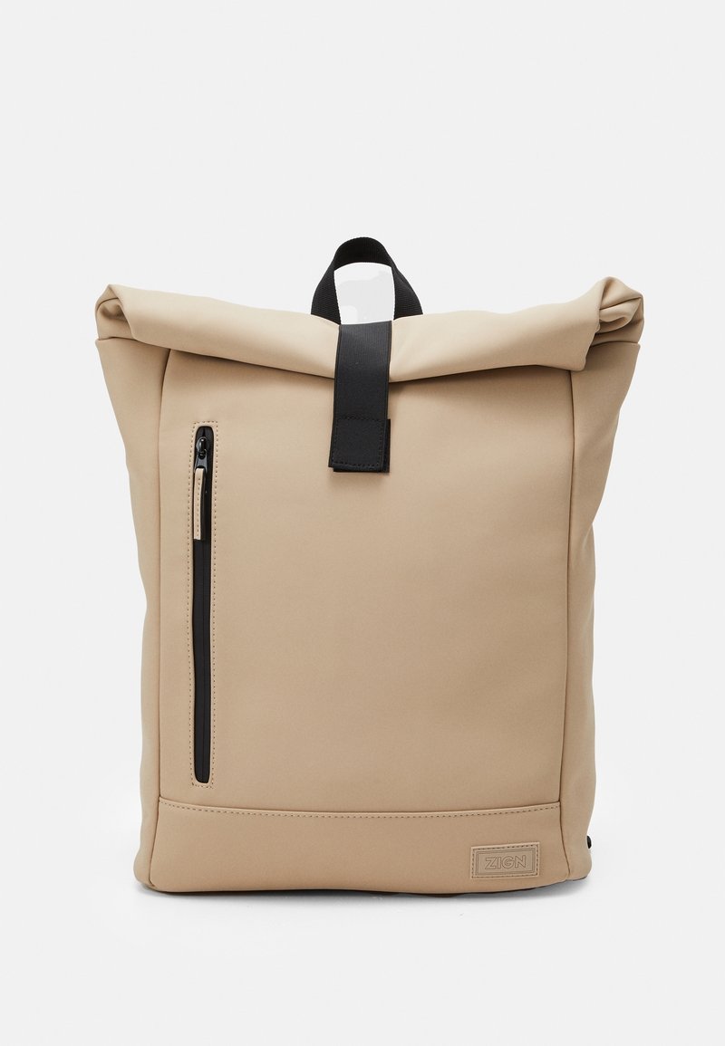 Sac à dos beige à rabat enroulable avec poche zippée noire sur le devant et poignée noire avec sangle, forme rectangulaire, design minimaliste.