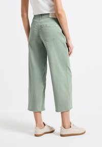 Pantalones cortos de pierna ancha en verde, confeccionados en tela suave, con dos bolsillos traseros y un ajuste casual, combinados con zapatillas ligeras.