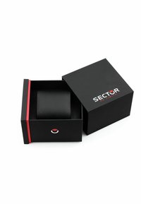 Scatola rettangolare nera con coperchio, caratterizzata da una striscia rossa e dal logo "SECTOR". All'interno della scatola si trova un oggetto cilindrico nero.